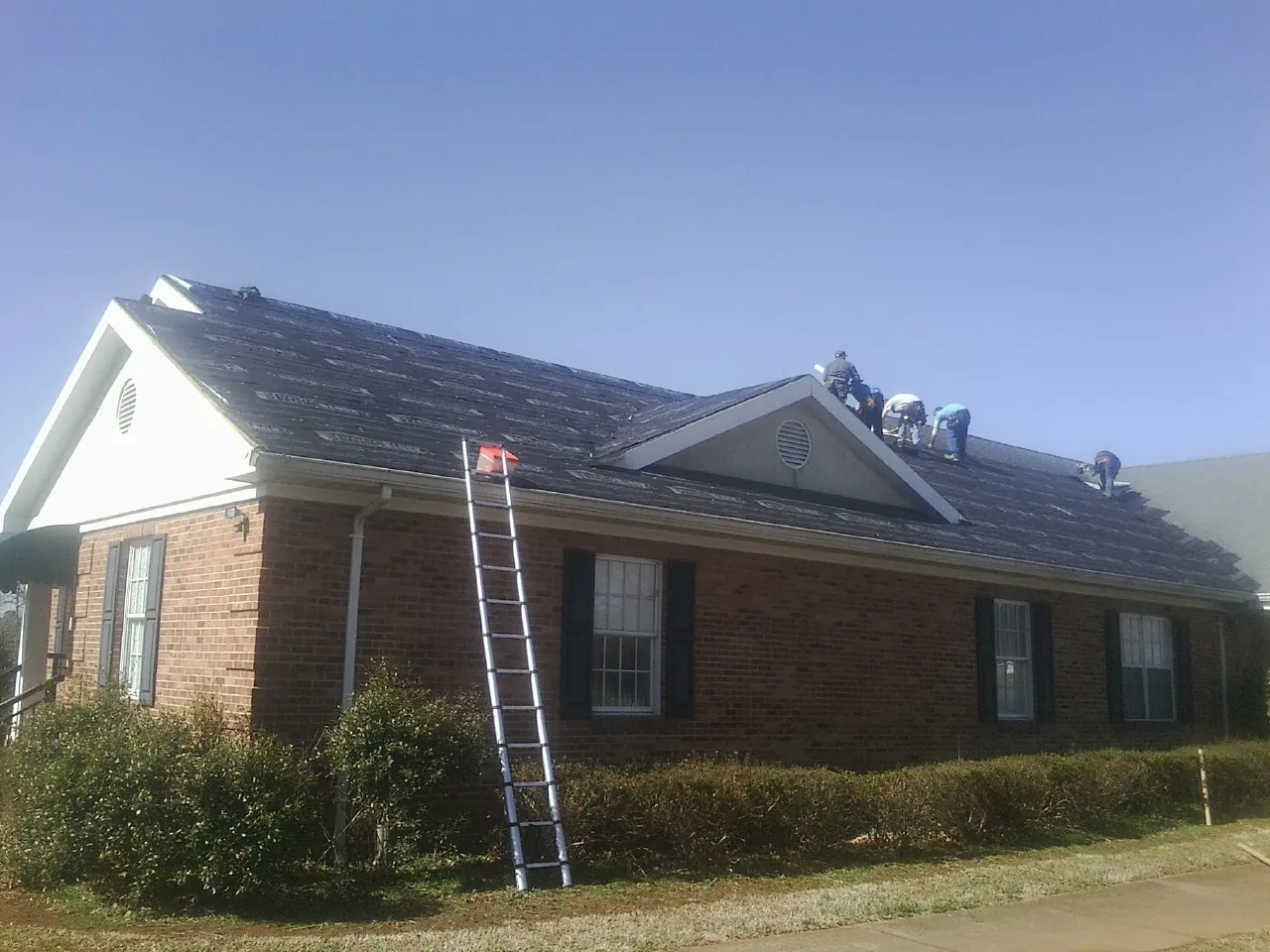 Crew tearing shingles off a brick ranch roof with a ladder set — Emergency Roof Repair work by our crew in Chippewa Lake
