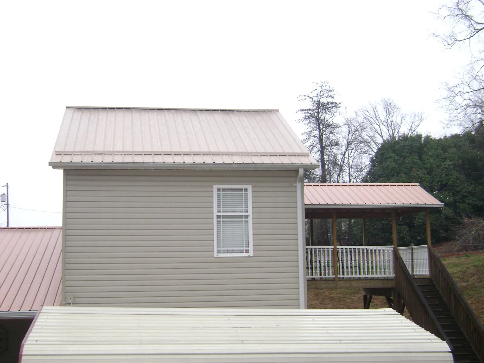 Tan metal roofs on a two story addition and attached porch, from a Roof Replacement job in Chippewa Lake